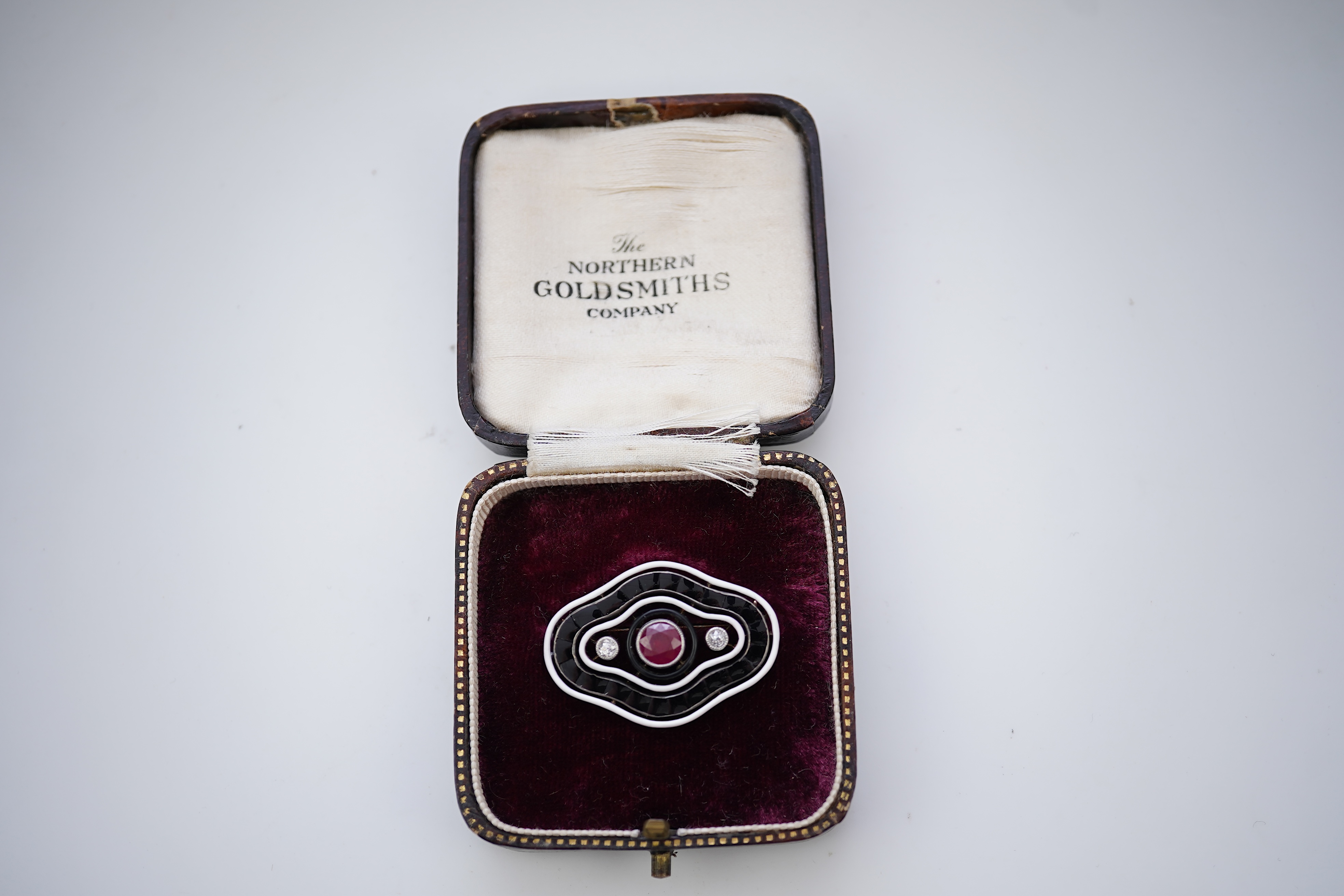 An unusual Art Deco onyx, enamel, ruby and diamond brooch, circa 1920